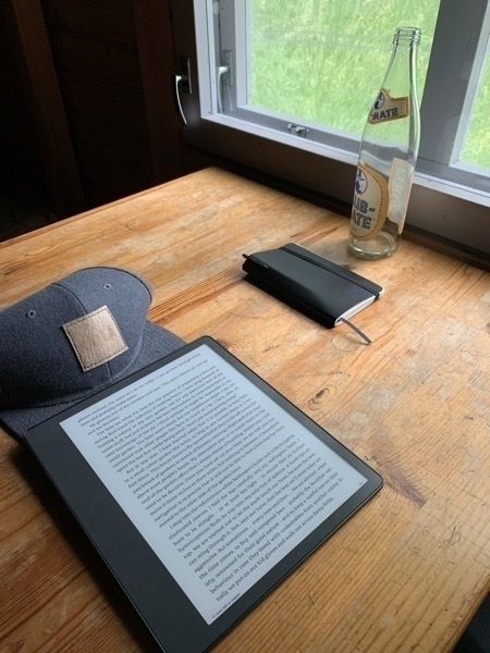 IMG_3757.jpeg A photo of table inside a cabin, on which are laying a few items: a base cap, an empty soda bottle (club mate), an ebook reader and a notebook with a strap holding it closed and a pen tucked inside it
