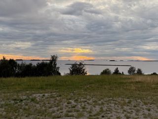 A photo of a cloudy sky over the coast near Oulu. In the middle of the photo, the sun is breaking through the otherwise grey-whitish clouds turning the sky orange-yellow. A ray of light seems to focus on one of the little islands scattered on the horizon.